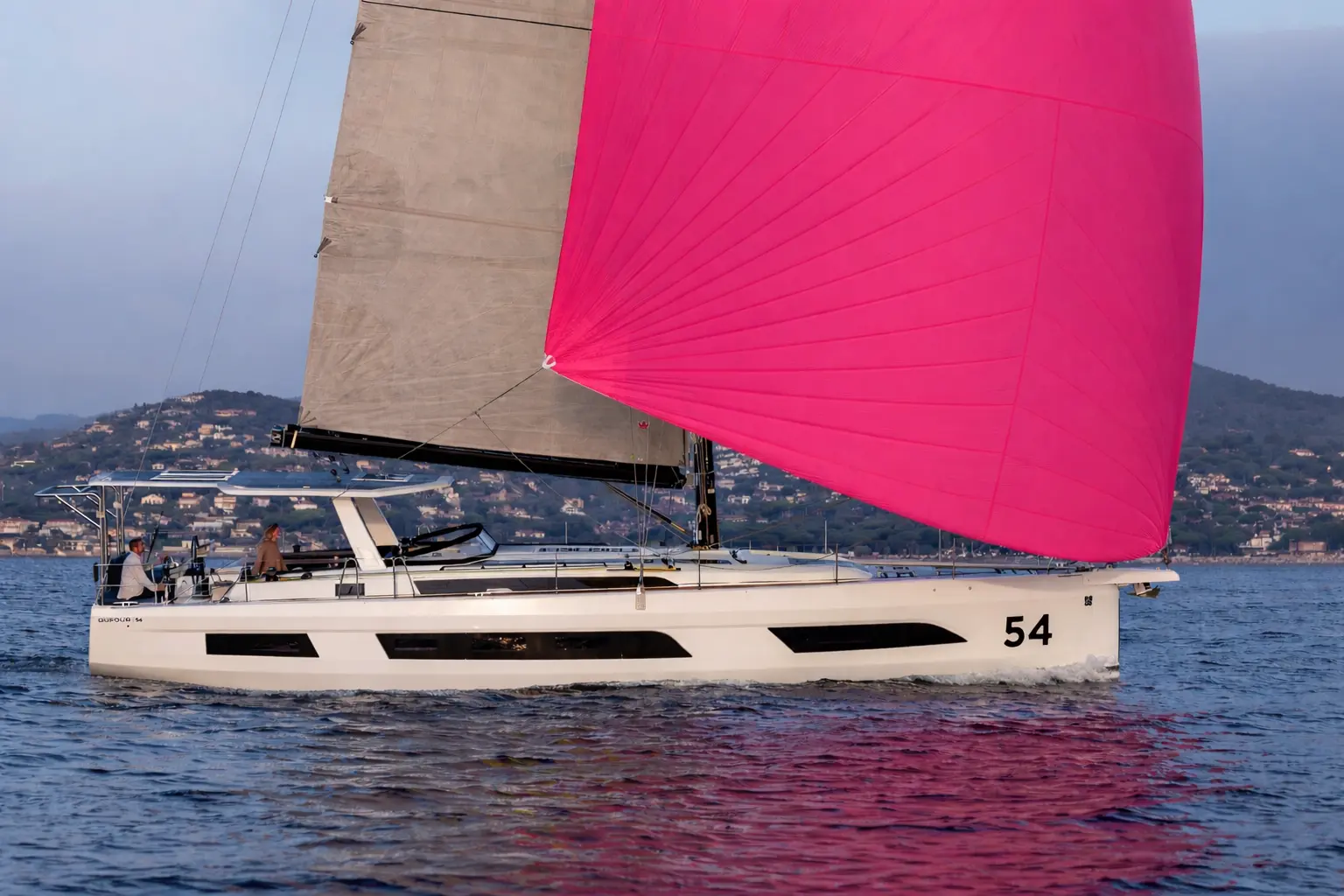 Hybrid Dufour 54 sailing with a pink spinnaker, cruising quietly along the coast with a focus on smooth navigation and onboard comfort