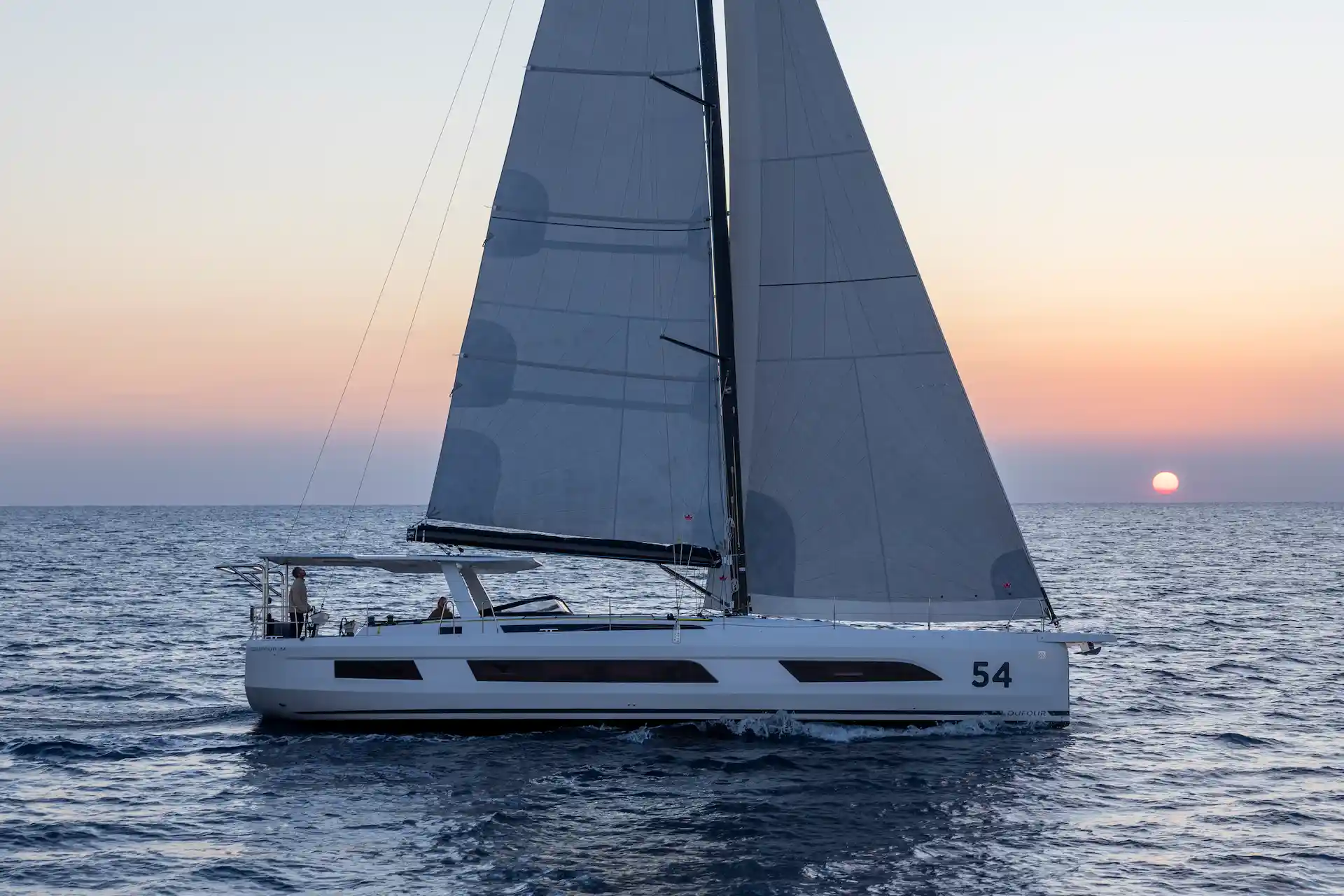Hybrid Dufour 54 sailing at sunset under full sail, offering a calm atmosphere, smooth motion, and a refined end-of-day cruising experience JOOOL