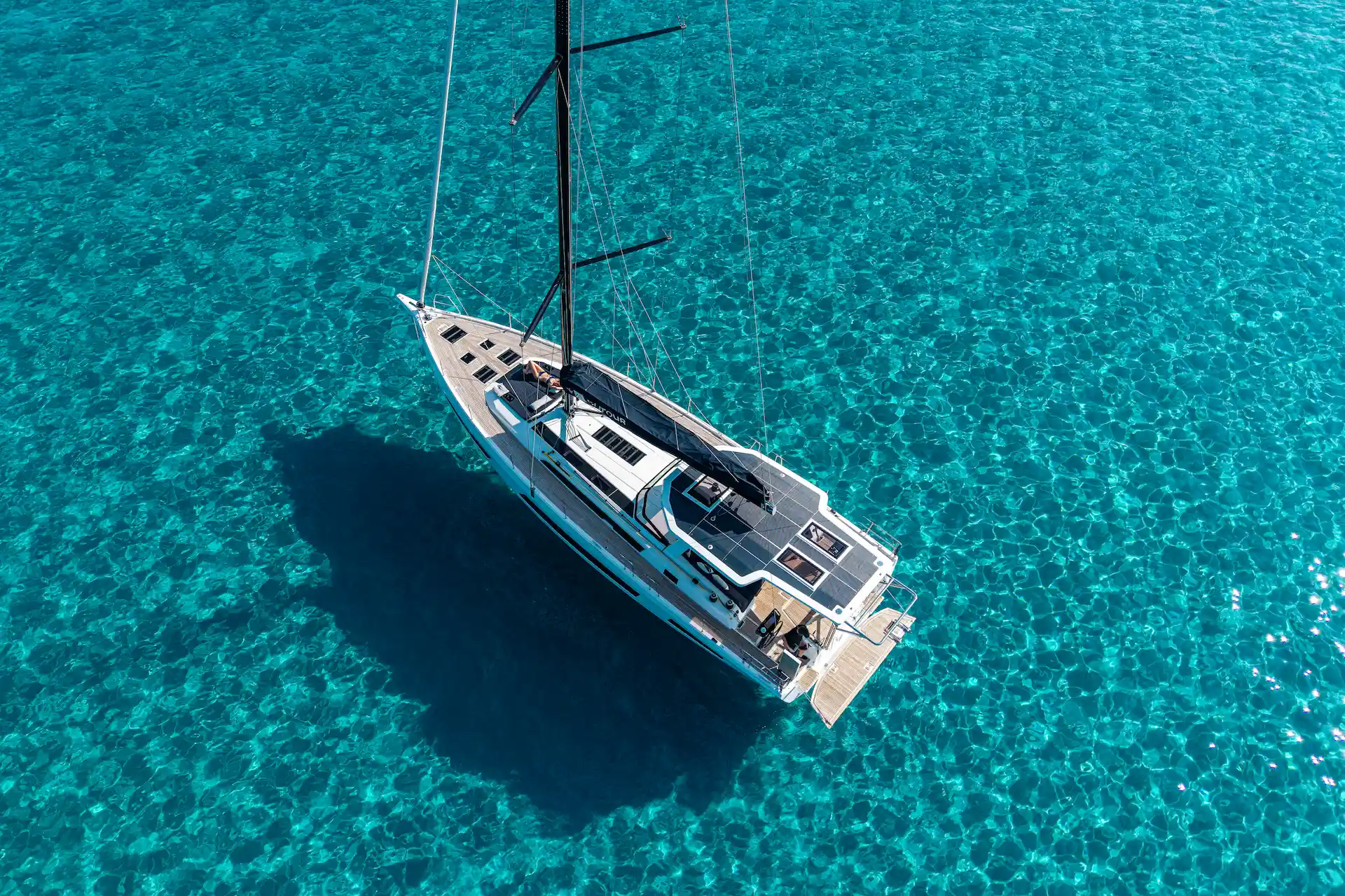 Hybrid Dufour 54 at anchor seen from above in clear turquoise water, highlighting calm surroundings, efficient onboard energy use, and relaxed cruising moments