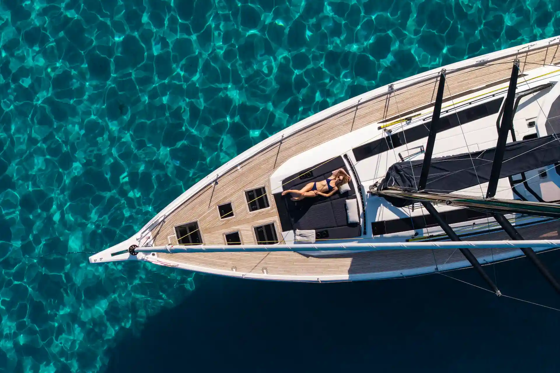 Hybrid Dufour 54 seen from above at anchor, with a guest relaxing on the foredeck above clear turquoise water, highlighting calm cruising and onboard comfort